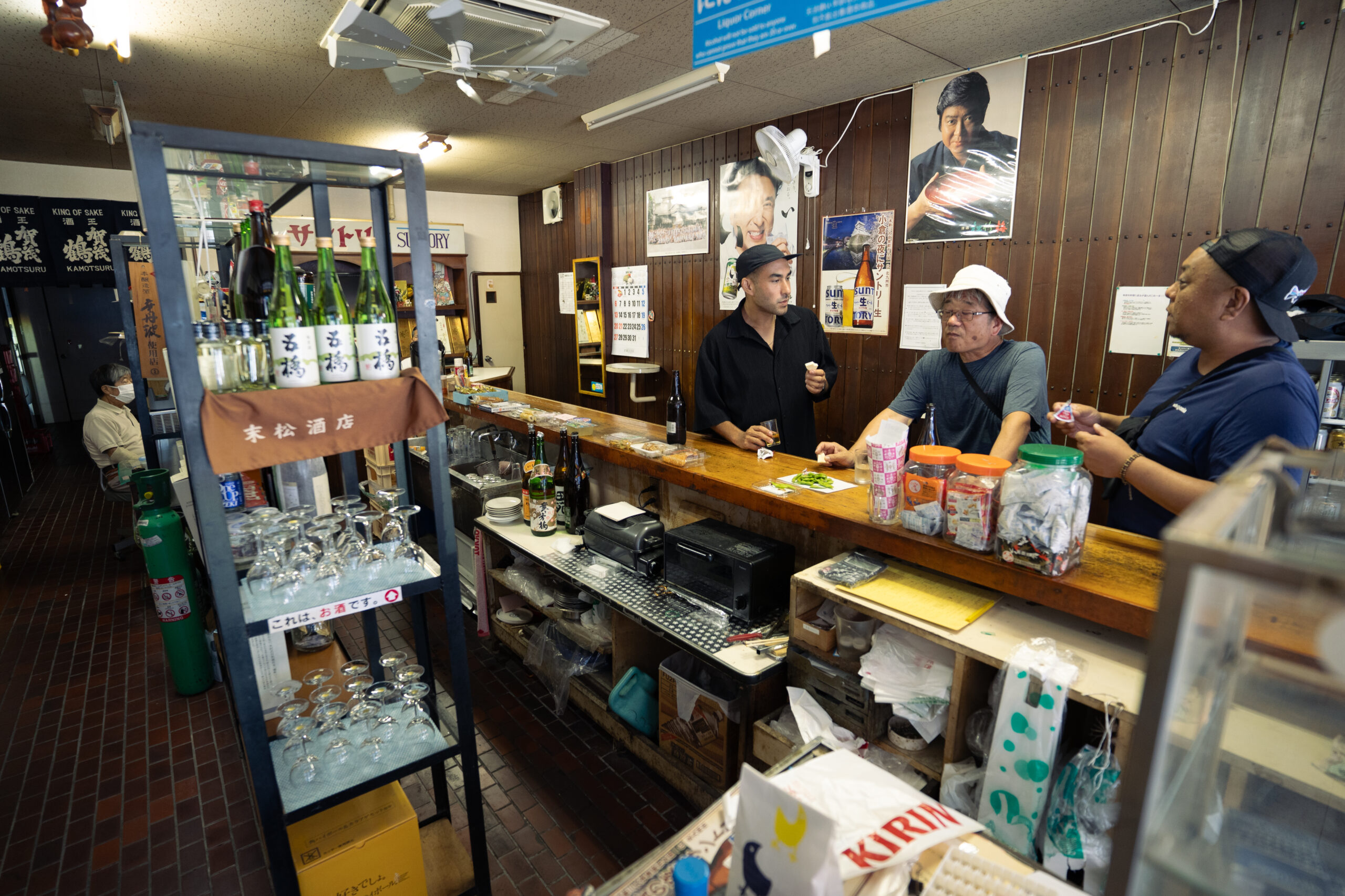 Interior view of a kakuchi liquor store in Kitakyushu, with a standing counter and local patrons enjoying drinks
